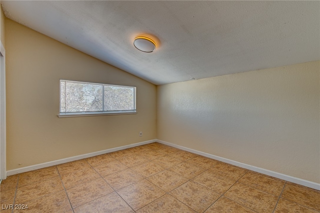 spare room with light tile patterned floors, a textured ceiling, and lofted ceiling