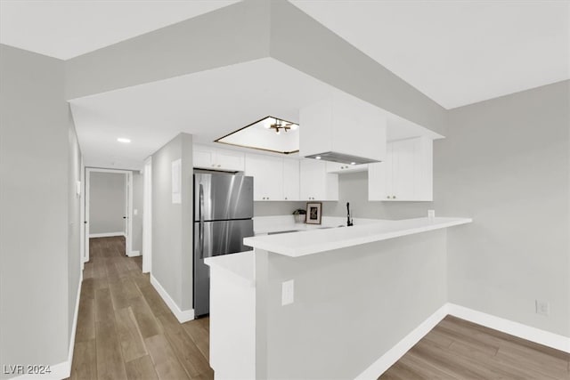 kitchen featuring kitchen peninsula, stainless steel fridge, white cabinetry, and light hardwood / wood-style flooring