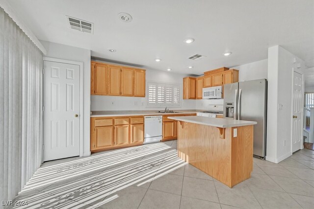 kitchen with a breakfast bar, a kitchen island, light tile patterned floors, and stainless steel appliances