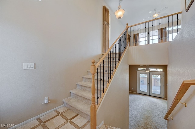 staircase with ceiling fan, plenty of natural light, carpet, and a high ceiling