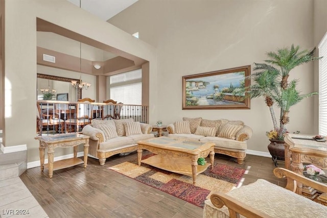 living room featuring a chandelier, a high ceiling, wood finish floors, visible vents, and baseboards