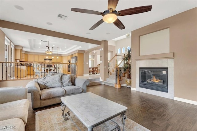 living room with a raised ceiling, a tiled fireplace, wood finished floors, baseboards, and stairs