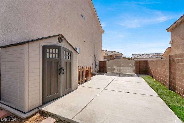 exterior space featuring a storage unit, stucco siding, a gate, fence, and an outdoor structure