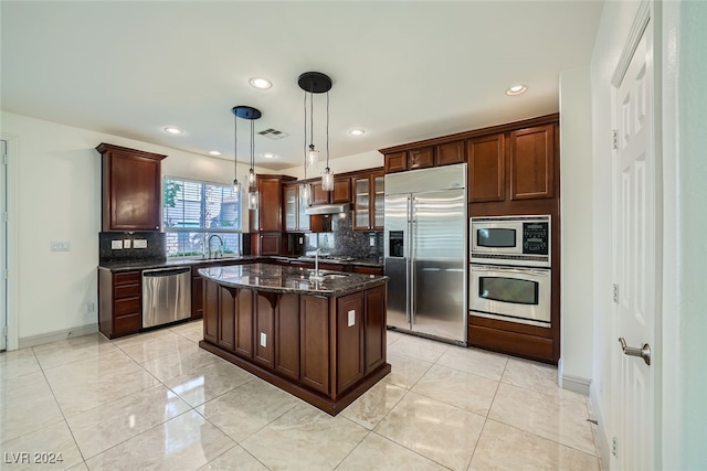 kitchen featuring built in appliances, decorative backsplash, a kitchen island with sink, and hanging light fixtures