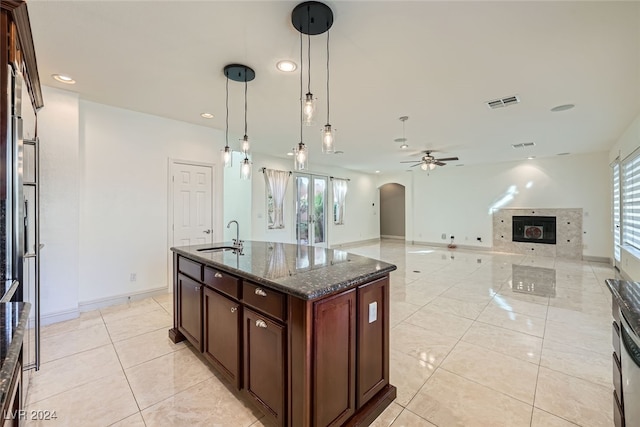 kitchen with ceiling fan, sink, dark stone countertops, decorative light fixtures, and a kitchen island with sink