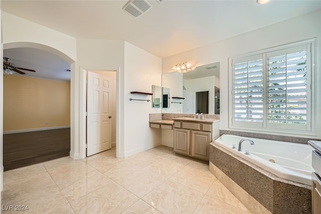 bathroom with tiled tub, ceiling fan, and vanity