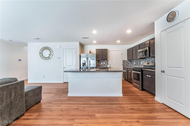 kitchen featuring appliances with stainless steel finishes, light wood-type flooring, backsplash, dark brown cabinets, and a center island with sink