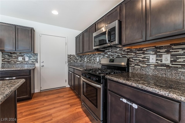 kitchen featuring stainless steel appliances, tasteful backsplash, dark stone countertops, dark brown cabinets, and hardwood / wood-style flooring