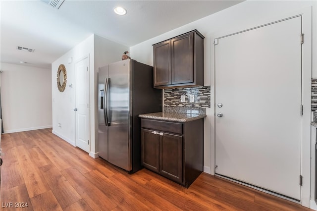 kitchen featuring stone countertops, backsplash, light hardwood / wood-style flooring, dark brown cabinets, and stainless steel fridge with ice dispenser