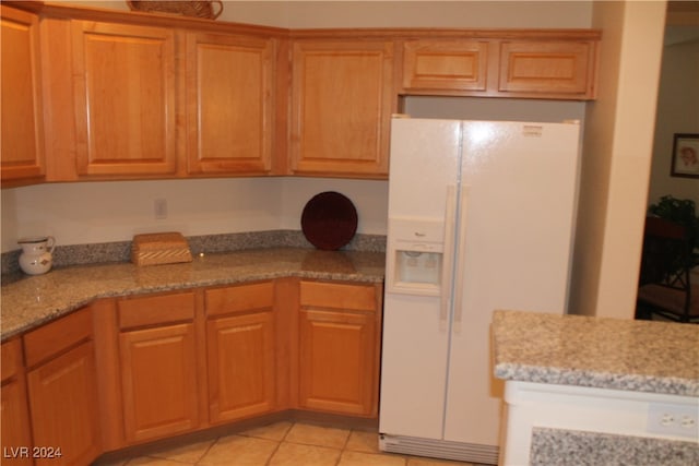 kitchen with light tile patterned flooring, light stone counters, and white fridge with ice dispenser