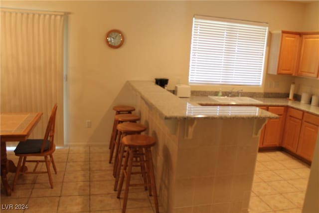 kitchen featuring a kitchen breakfast bar, light tile patterned flooring, sink, and light brown cabinets