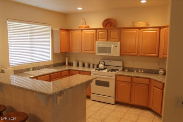 kitchen with sink, kitchen peninsula, white appliances, a breakfast bar, and light tile patterned flooring