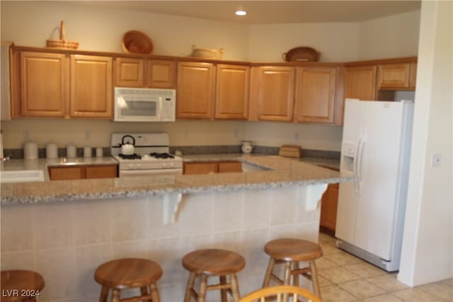 kitchen featuring a kitchen bar, kitchen peninsula, light stone countertops, white appliances, and light tile patterned flooring