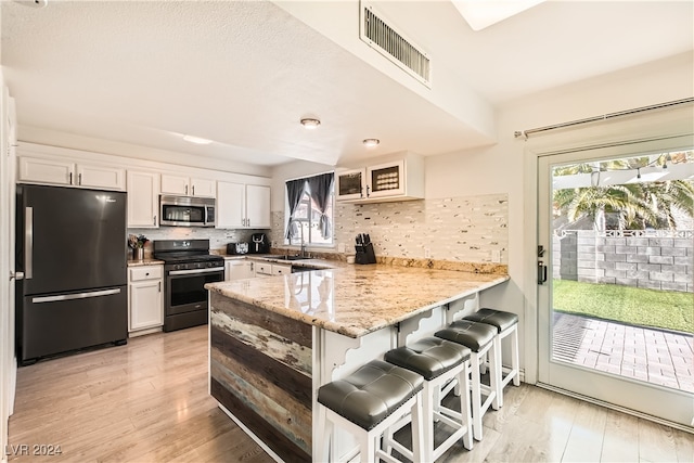 kitchen featuring white cabinets, a kitchen bar, kitchen peninsula, and appliances with stainless steel finishes