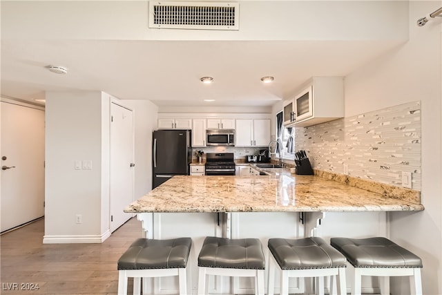 kitchen featuring sink, appliances with stainless steel finishes, tasteful backsplash, light hardwood / wood-style floors, and kitchen peninsula