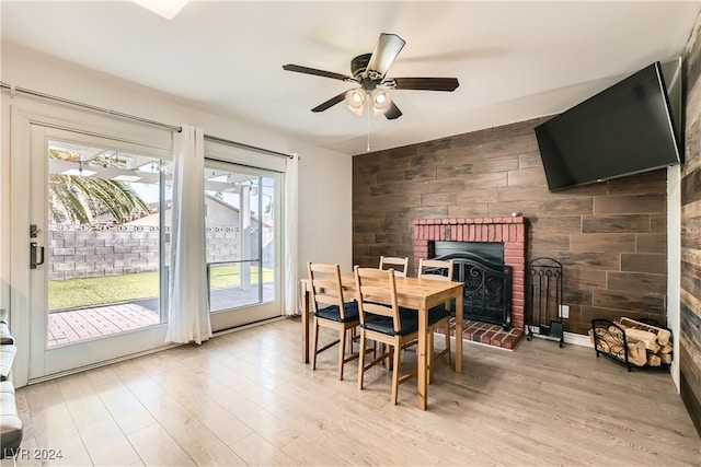 dining space with wood walls, ceiling fan, a healthy amount of sunlight, and a brick fireplace