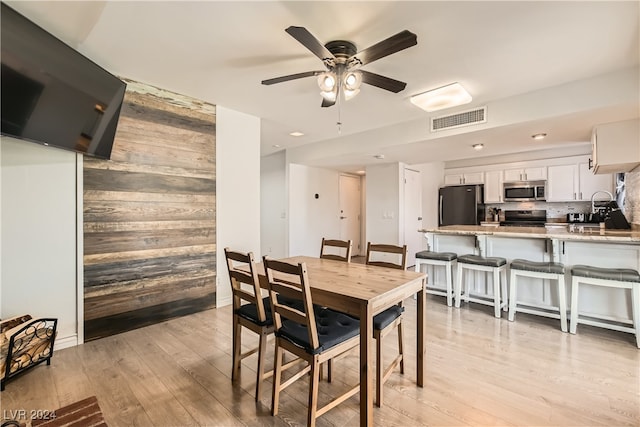 dining area featuring wooden walls, ceiling fan, and light hardwood / wood-style floors