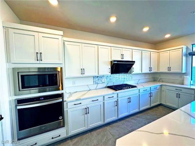 kitchen with stainless steel appliances, light stone counters, dark tile patterned floors, white cabinets, and exhaust hood