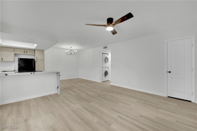 unfurnished living room with ceiling fan with notable chandelier, light wood-type flooring, and stacked washer and clothes dryer