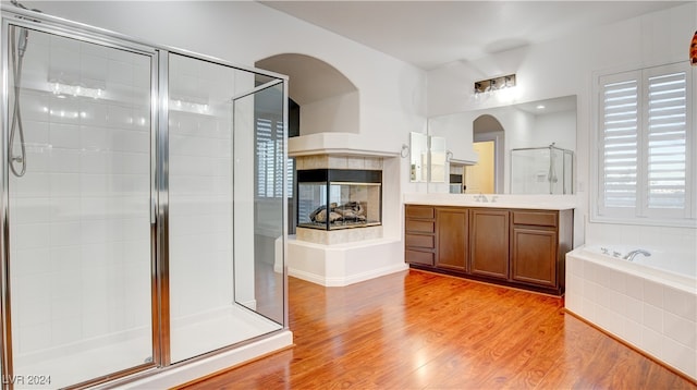 bathroom with vanity, wood-type flooring, shower with separate bathtub, and a tiled fireplace