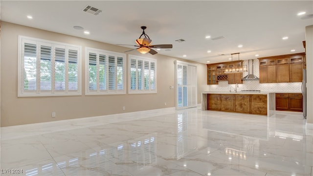 kitchen featuring backsplash, ceiling fan, wall chimney range hood, and hanging light fixtures