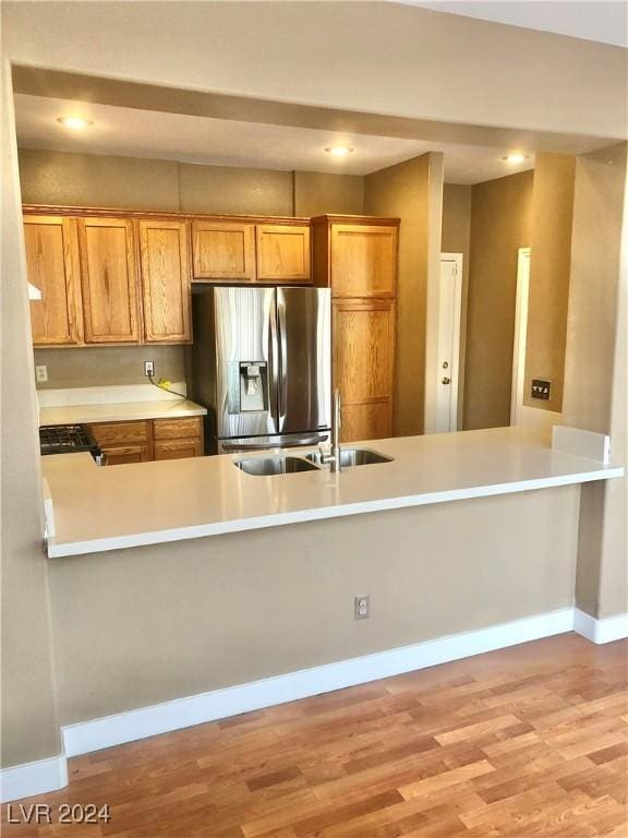 kitchen with kitchen peninsula, stainless steel refrigerator with ice dispenser, light wood-type flooring, and sink