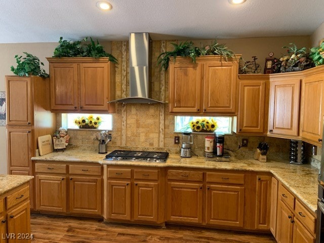 kitchen with backsplash, wall chimney exhaust hood, a textured ceiling, stainless steel gas cooktop, and wood-type flooring