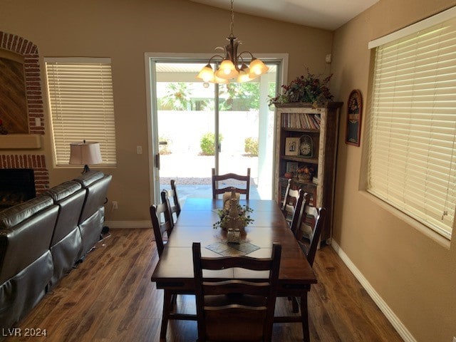 dining room featuring a notable chandelier, a fireplace, dark wood-type flooring, and vaulted ceiling