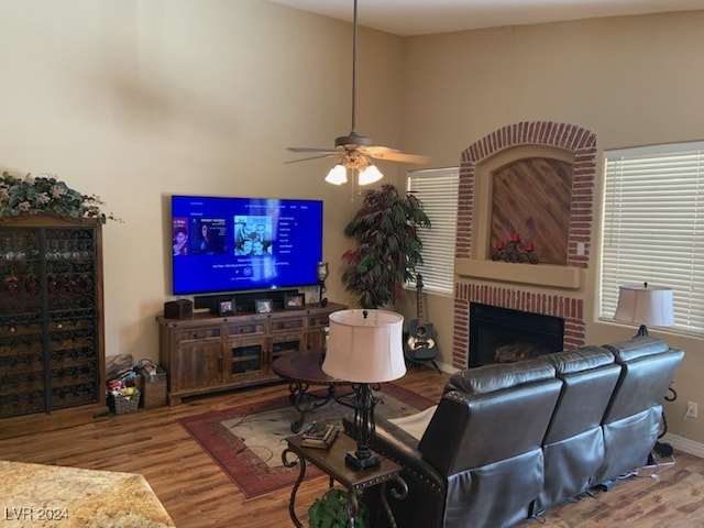 living room with hardwood / wood-style flooring, ceiling fan, a towering ceiling, and a brick fireplace