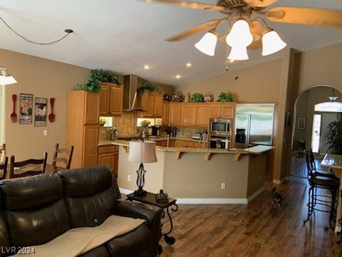 kitchen featuring a kitchen island with sink, a kitchen breakfast bar, wall chimney exhaust hood, dark hardwood / wood-style floors, and appliances with stainless steel finishes