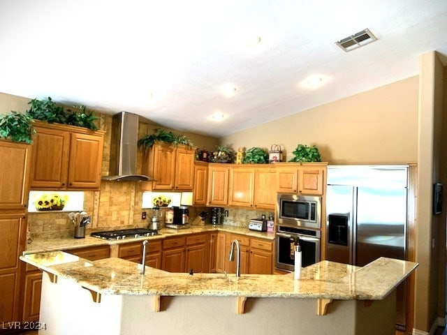 kitchen featuring wall chimney range hood, built in appliances, a breakfast bar area, decorative backsplash, and a kitchen island