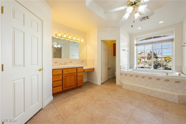 bathroom with vanity, tile patterned flooring, ceiling fan, a relaxing tiled tub, and toilet