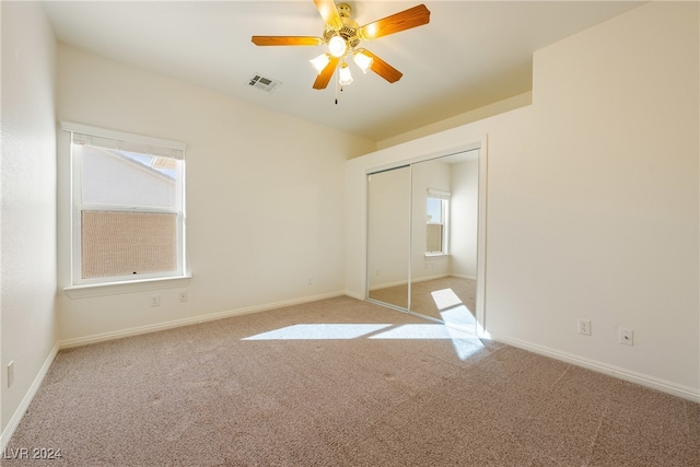 unfurnished bedroom with ceiling fan, a closet, light carpet, and multiple windows