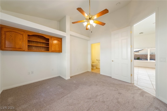 unfurnished bedroom with a towering ceiling, connected bathroom, light colored carpet, and ceiling fan