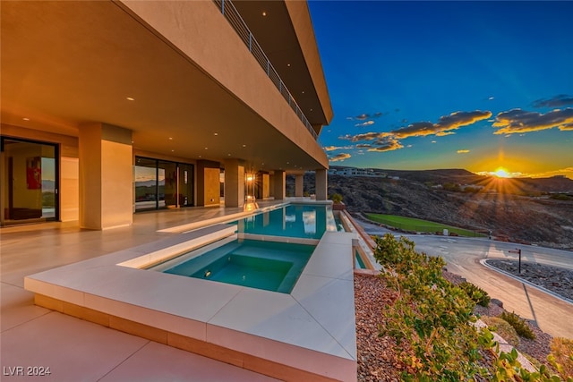 pool at dusk with a patio area, an in ground hot tub, and a mountain view