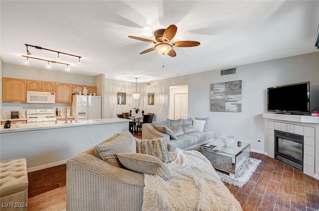 living room with a tiled fireplace, ceiling fan, sink, and dark hardwood / wood-style floors