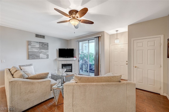 living room with a fireplace, ceiling fan, and dark wood-type flooring