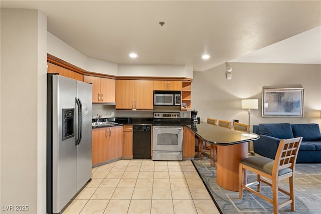 kitchen with dark countertops, open floor plan, a peninsula, stainless steel appliances, and a sink