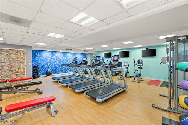 exercise room with a drop ceiling, visible vents, baseboards, and wood finished floors