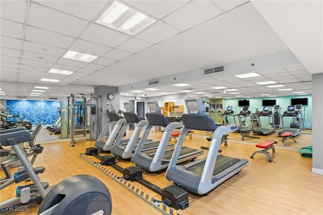 exercise room with a drop ceiling, wood finished floors, and visible vents