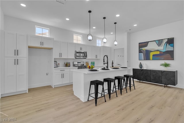 kitchen with stainless steel appliances, white cabinetry, hanging light fixtures, and a center island with sink