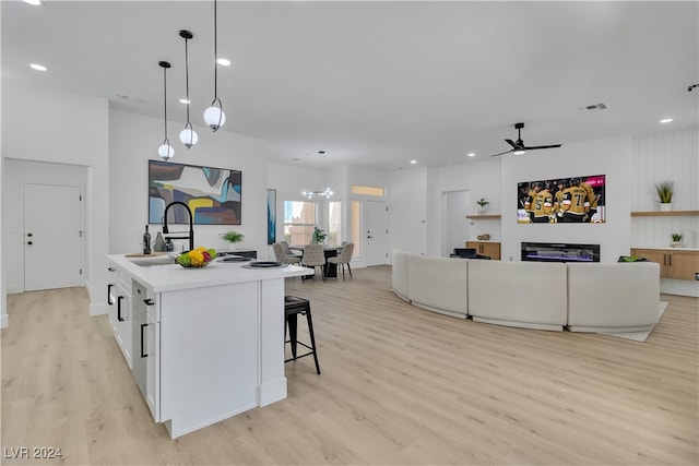 kitchen with a kitchen island with sink, sink, decorative light fixtures, and light hardwood / wood-style flooring