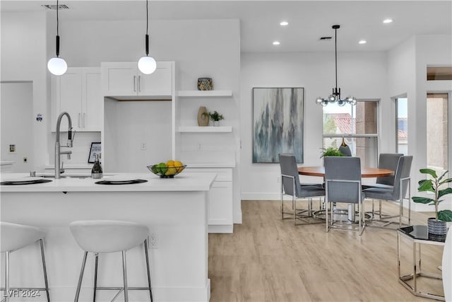 kitchen with white cabinets, light hardwood / wood-style flooring, hanging light fixtures, and a notable chandelier