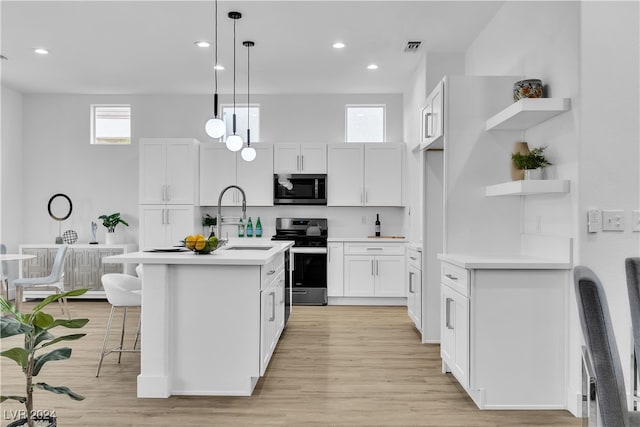 kitchen with appliances with stainless steel finishes, a kitchen island with sink, sink, pendant lighting, and white cabinetry