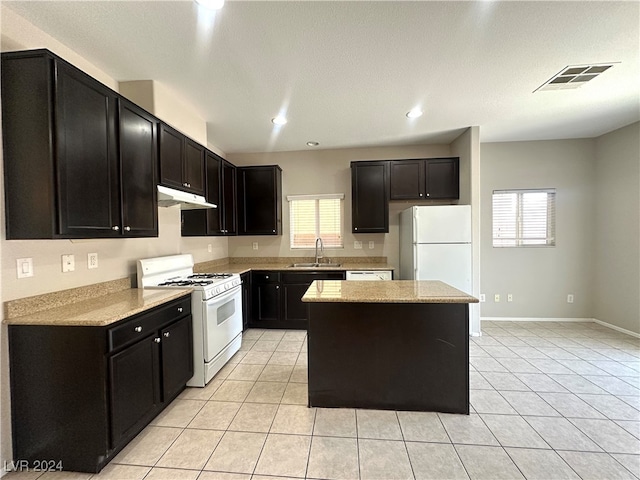 kitchen featuring light stone countertops, white appliances, sink, a kitchen island, and light tile patterned flooring