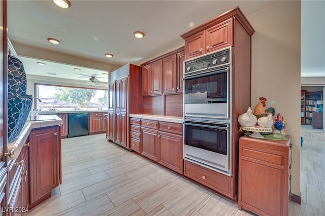 kitchen featuring sink, light hardwood / wood-style floors, tile counters, and black appliances