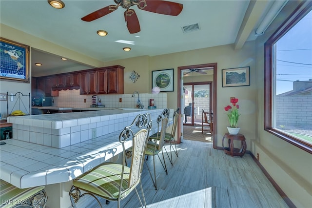 kitchen with tile counters, sink, beamed ceiling, kitchen peninsula, and decorative backsplash