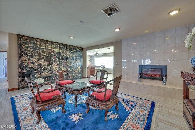 living room featuring a tiled fireplace, ceiling fan, and tile walls