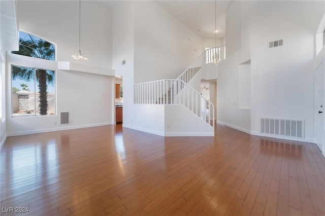 unfurnished living room featuring a high ceiling, hardwood / wood-style flooring, and an inviting chandelier