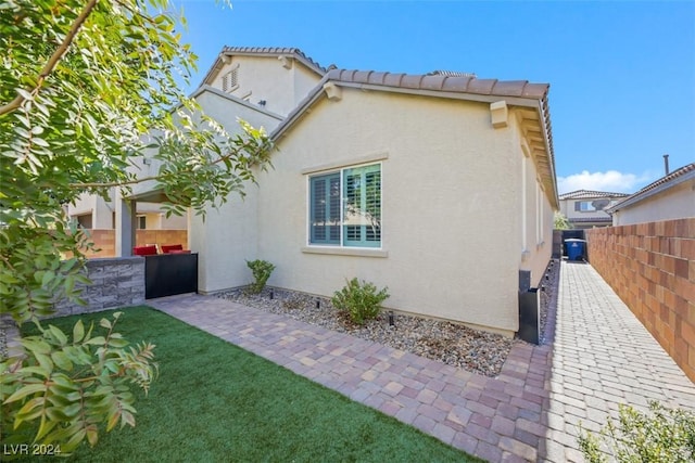 view of home's exterior with stucco siding, a tile roof, a patio, fence, and a yard